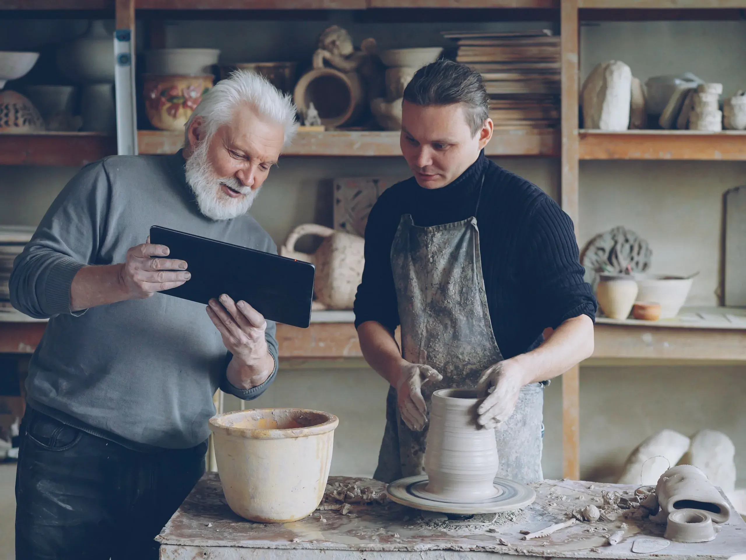Formateur une tablette en main, guidant un adulte en apprentissage au tour dans un atelier de céramique